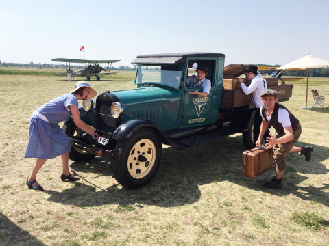 Lotta Stein kurbelt ein historisches Auto an, während Robert Nippoldt, Philip Ritter und Christoph Kopp letzte Koffer einladen